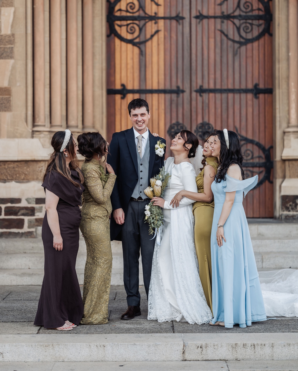 adelaide's st peter's cathedral wedding - irish & nick 39 Wedding party portrait outside historic stone venue with bride, groom, and bridesmaids.