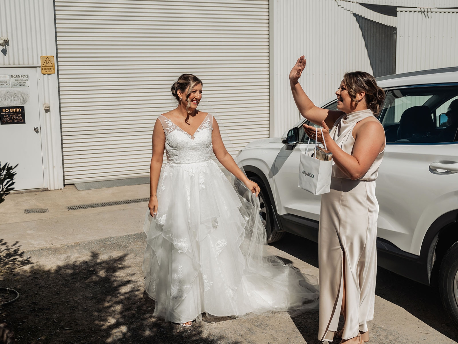 lloyd brothers wedding - dajana & tom 6 Bride and guest in elegant dresses share joyful moment at sunny wedding venue.