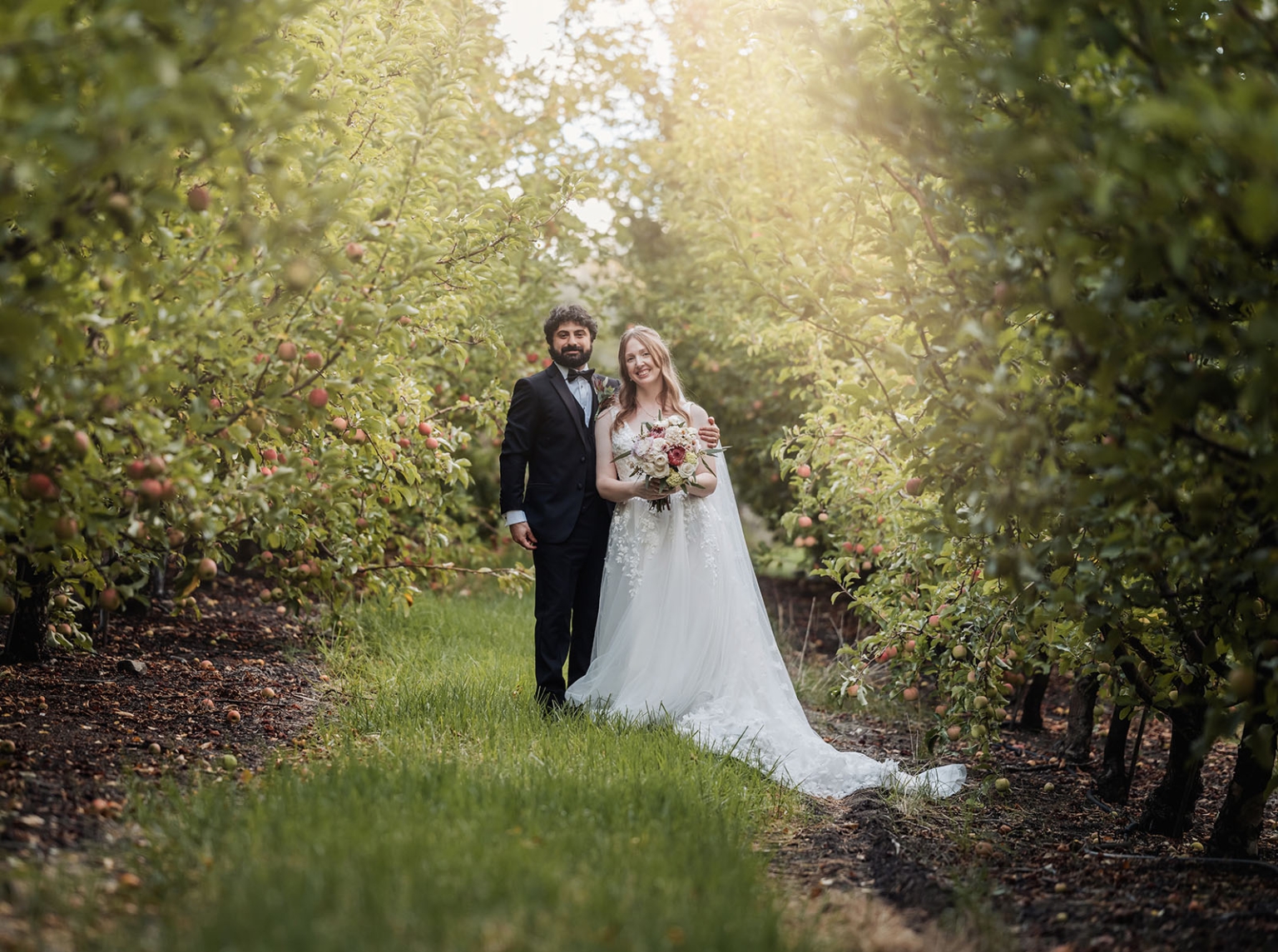 beautiful manor basket range wedding - sophie & theodore 127 Bride and groom in an apple orchard, sunlight filtering through trees, creating a romantic scene.