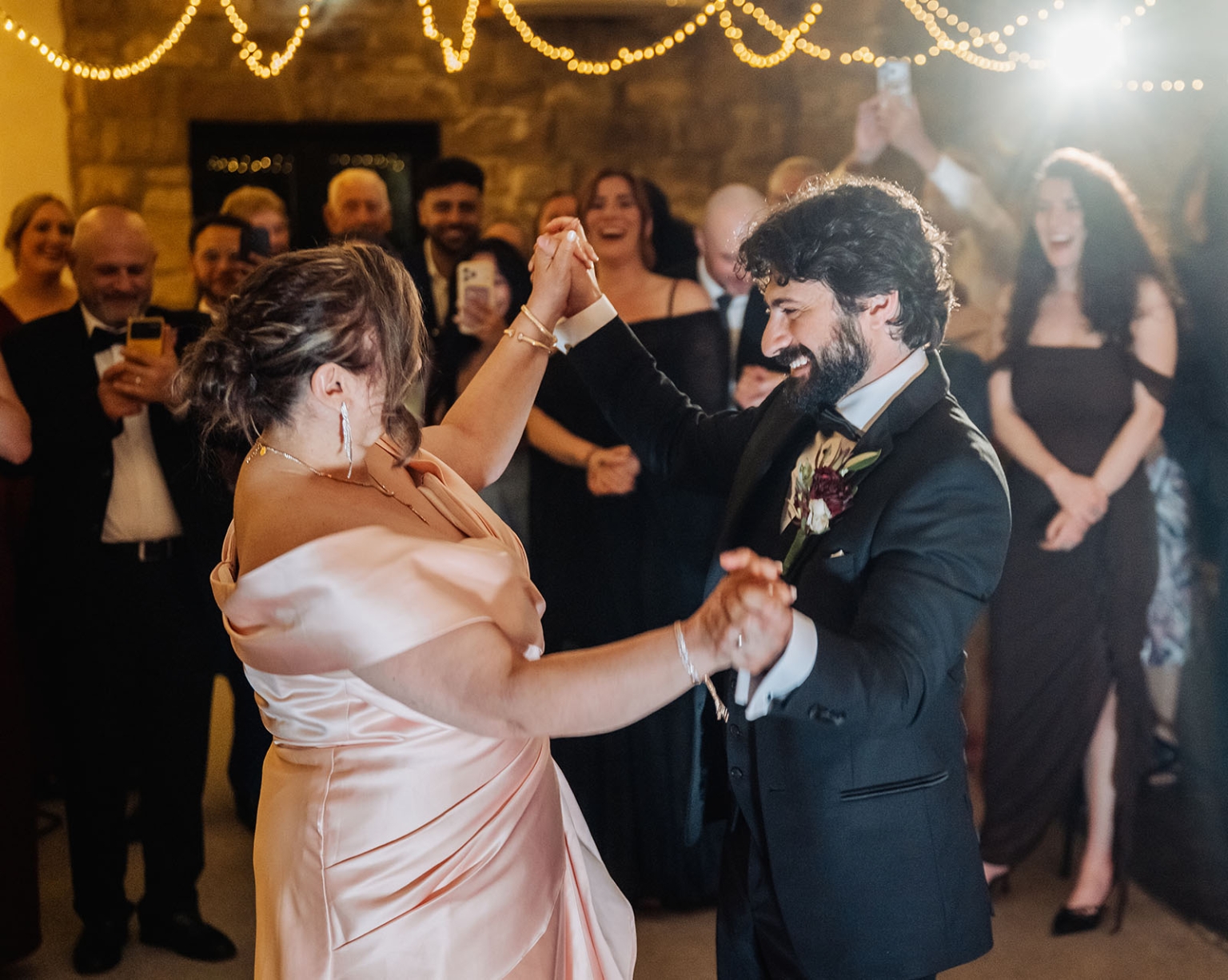 beautiful manor basket range wedding - sophie & theodore 147 Wedding couple dancing at elegant reception with cheering guests and fairy lights.