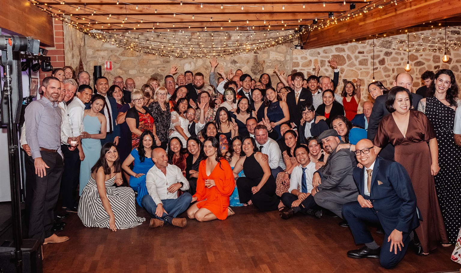 adelaide hills wedding at the manor - jo & dan 74 Joyful wedding reception group photo in rustic venue with string lights.
