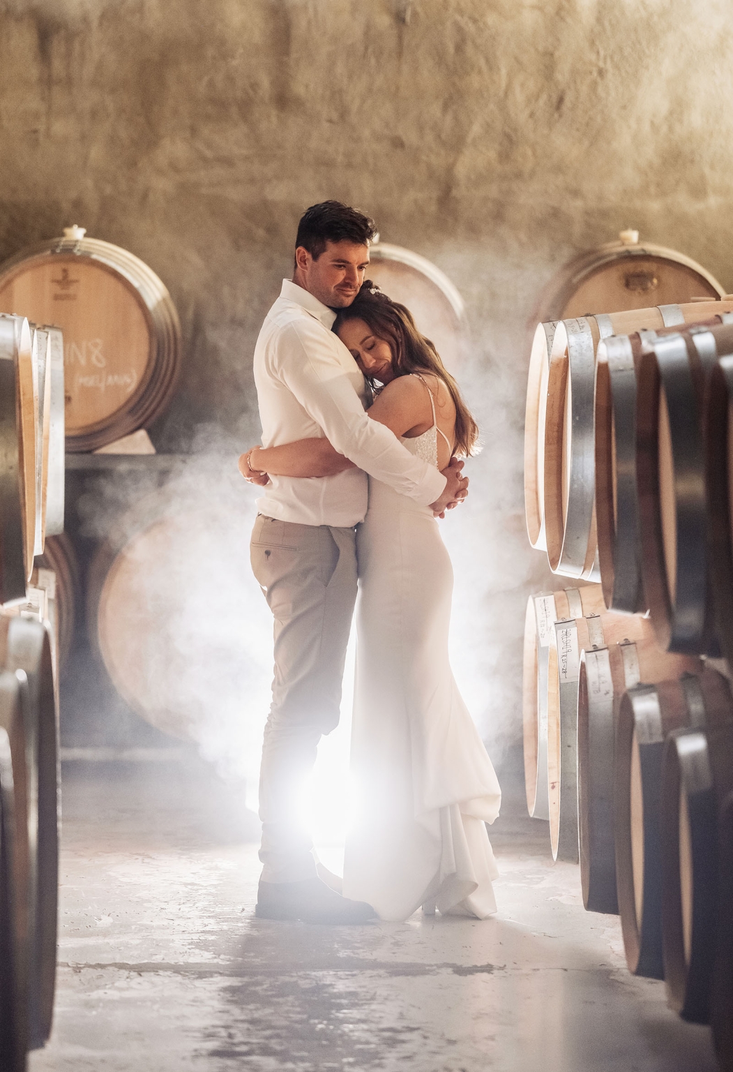 the lane vineyard wedding - caitlyn & craig 127 Romantic couple embracing in a rustic wine cellar with barrels and soft lighting.