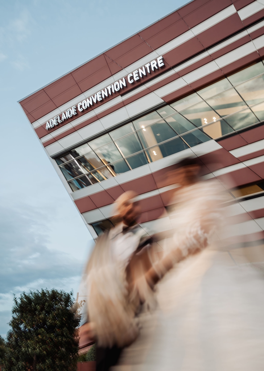 st george & st shenouda coptic church wedding - carmina & bill 78 Adelaide Convention Centre exterior with modern facade and blurred pedestrians.