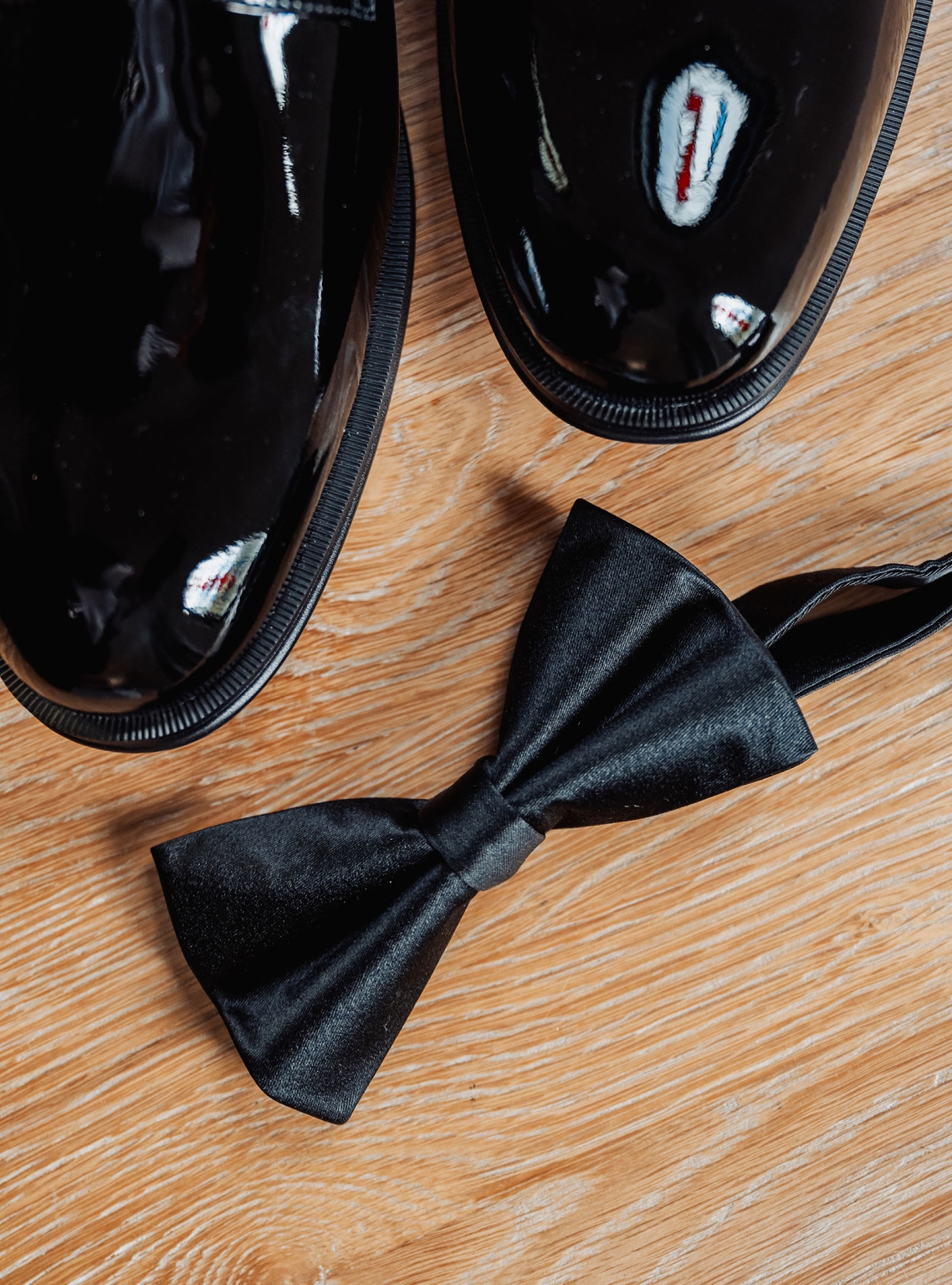 the manor wedding - crystal & mackenzie 2 Black patent leather dress shoes and satin bow tie on wood floor.