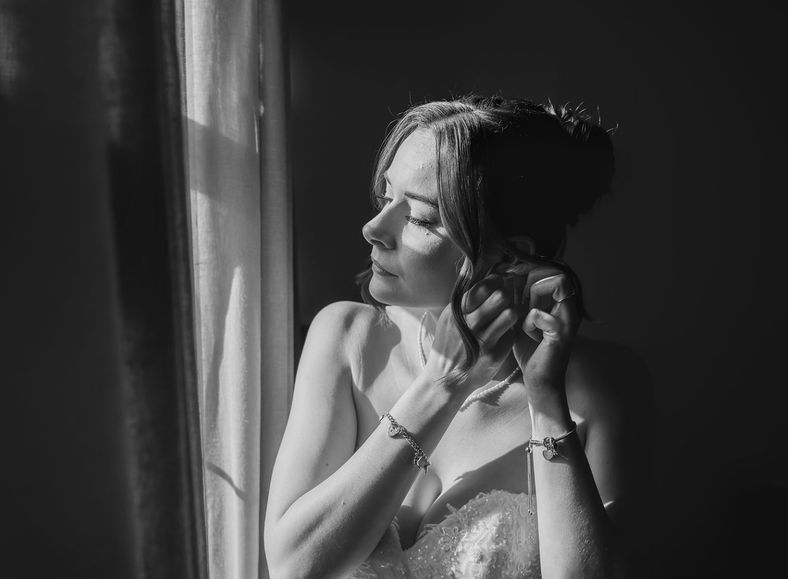 the manor wedding - crystal & mackenzie 19 Bride adjusting earring by window in dramatic black and white wedding portrait.