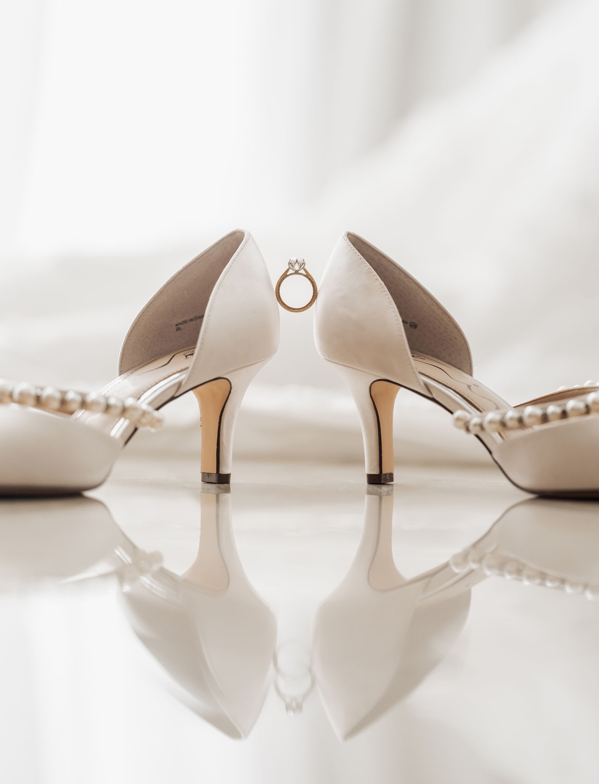 st george & st shenouda coptic church wedding - carmina & bill 19 Ivory bridal heels with gold engagement ring on reflective wedding surface.