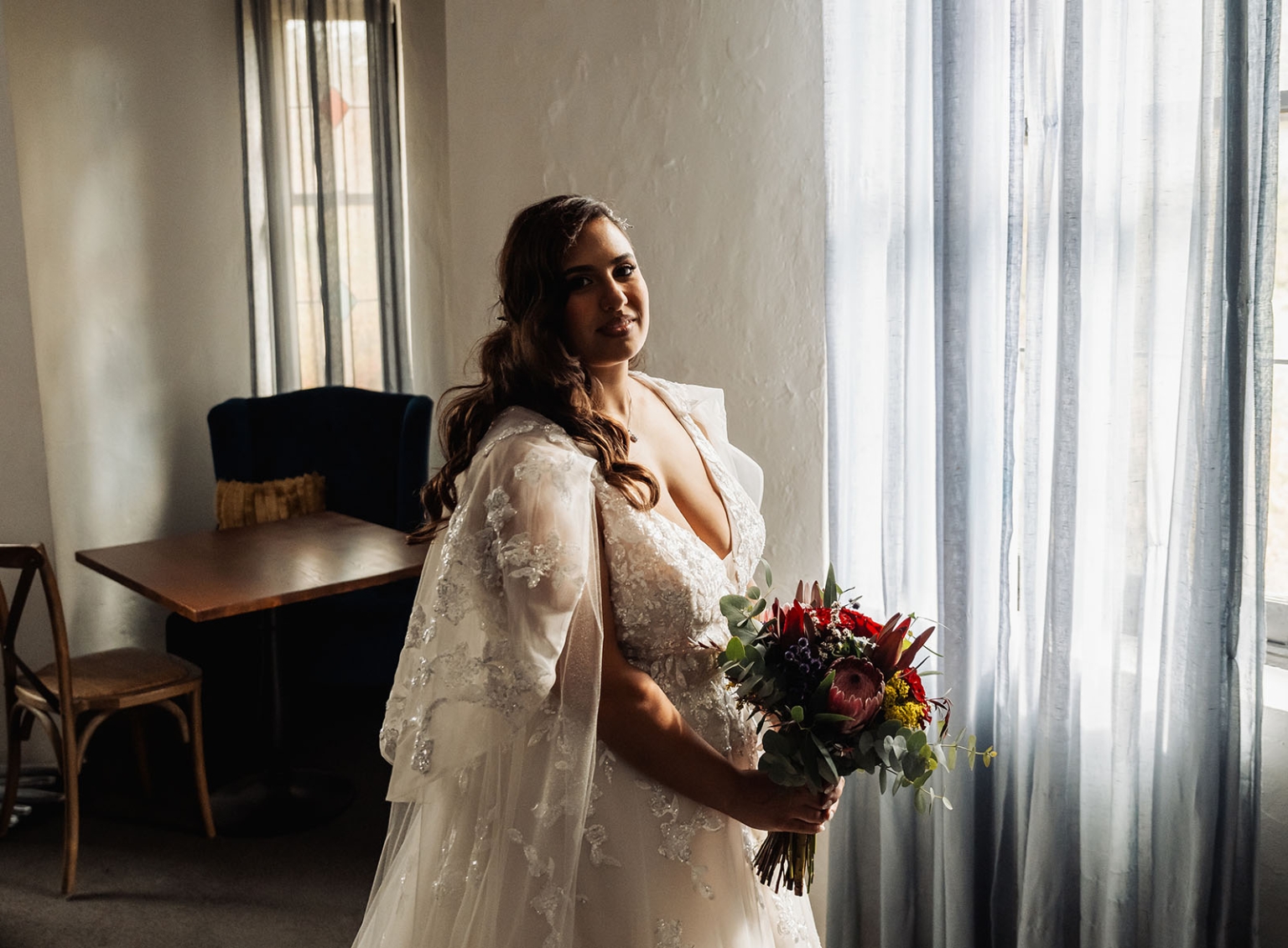 basket range wedding at the manor - leah & wes 9 Bride in embroidered wedding gown holding burgundy bouquet by softly lit window.