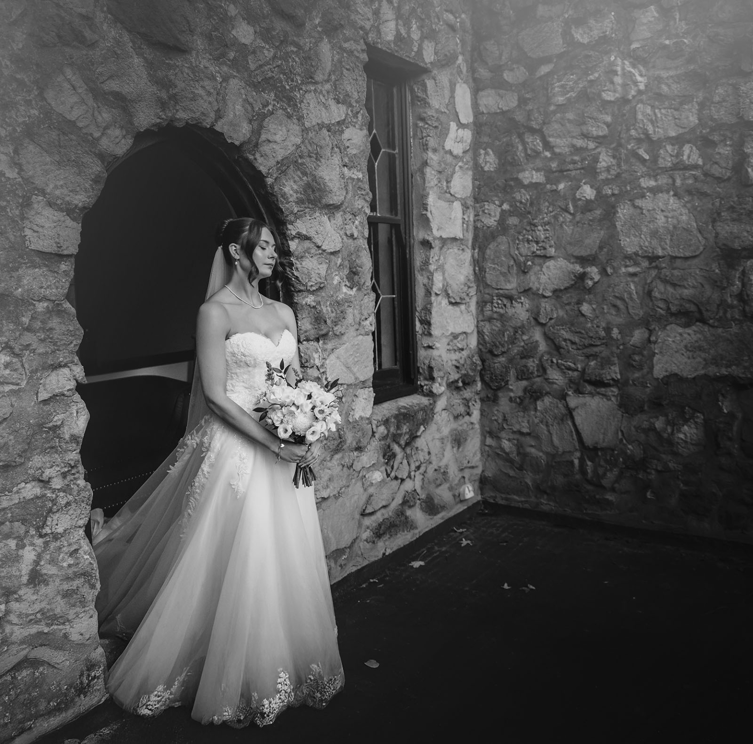 the manor wedding - crystal & mackenzie 38 Black-and-white bridal portrait with wedding gown and bouquet by rustic stone arch.