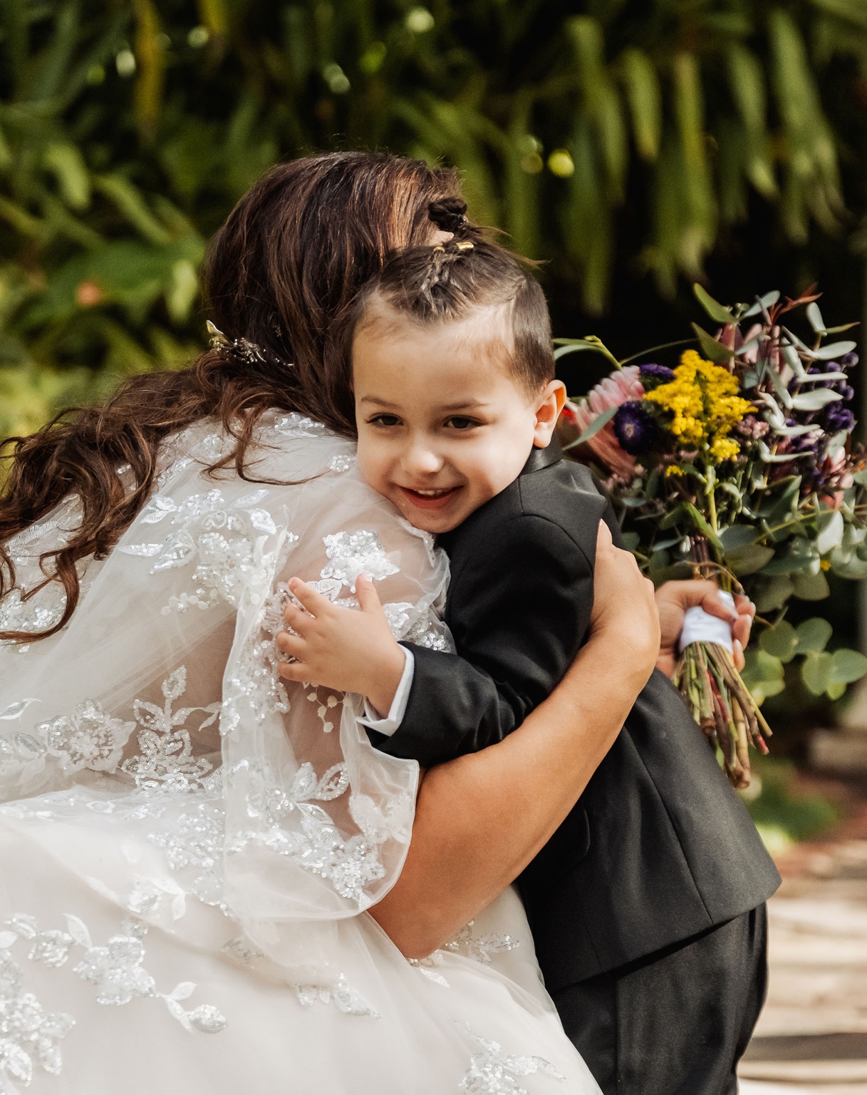 basket range wedding at the manor - leah & wes 36 Bride hugging young boy during outdoor wedding ceremony with colorful bouquet.