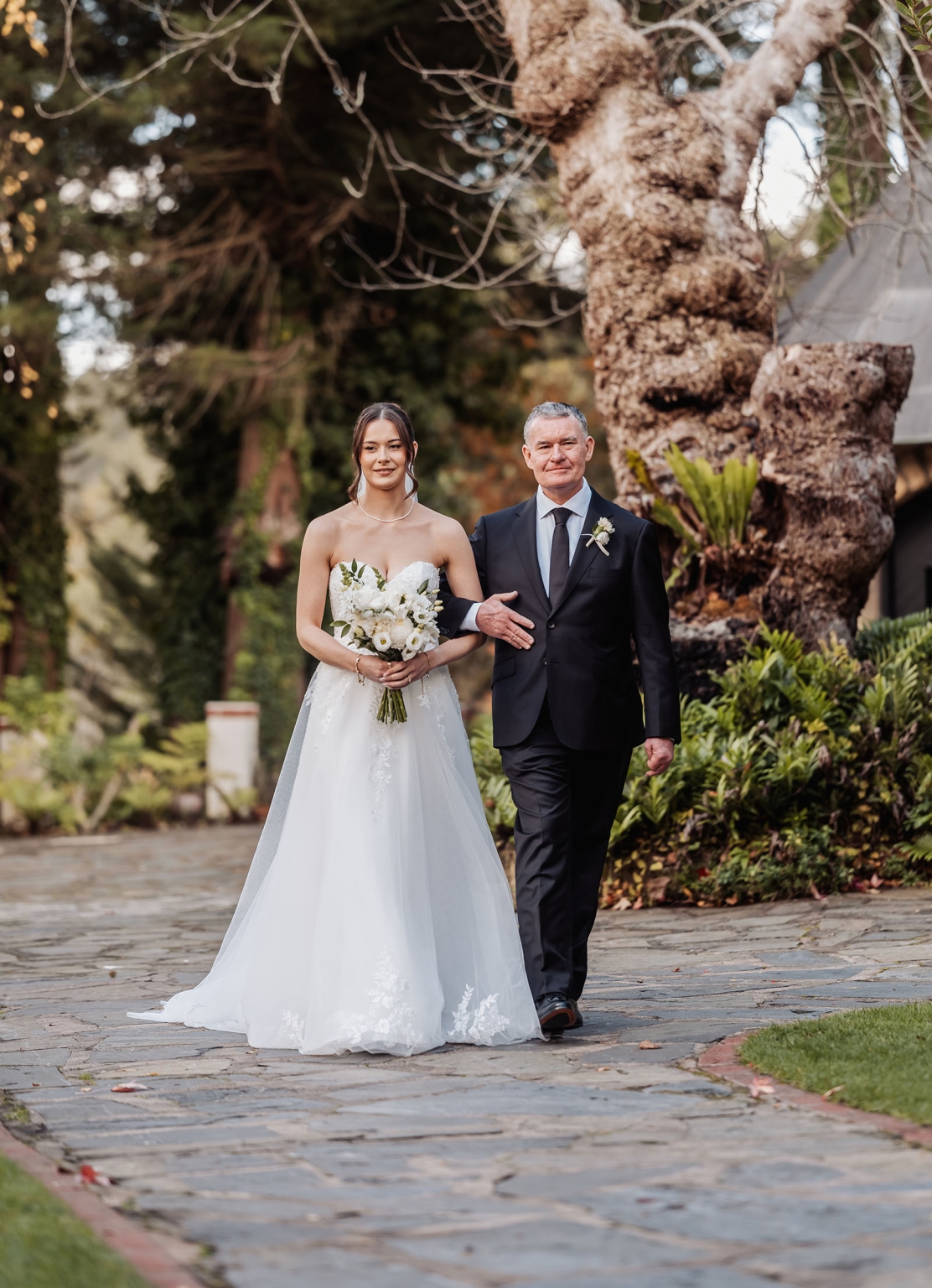 the manor wedding - crystal & mackenzie 47 Bride escorted down garden wedding path with white bouquet.