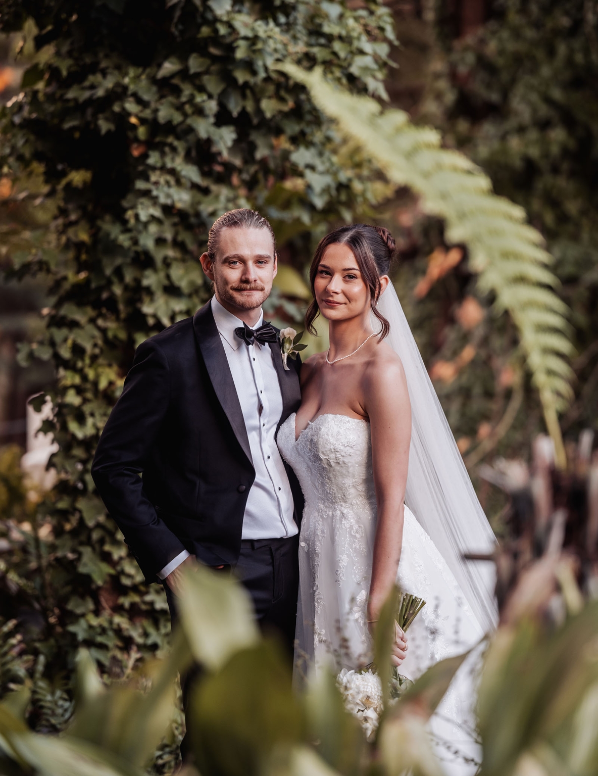 the manor wedding - crystal & mackenzie 65 Bride and groom wedding portrait in lush garden with elegant tuxedo and lace gown.