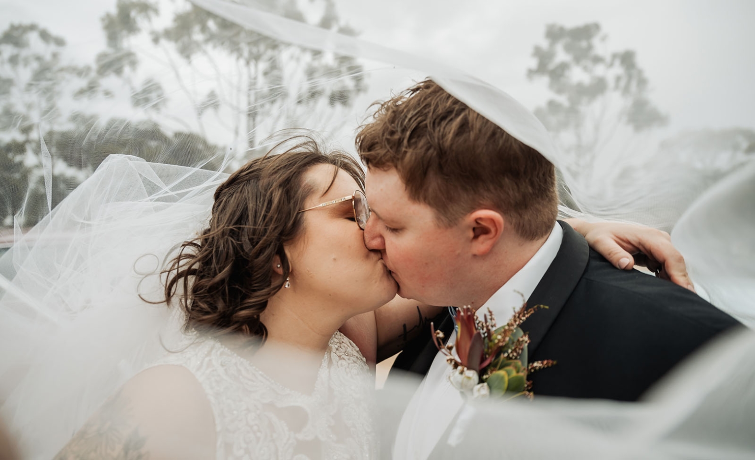 loxton's st peter's church wedding - madeline & brayden 46 Bride and groom kissing under windblown wedding veil during romantic outdoor portrait.
