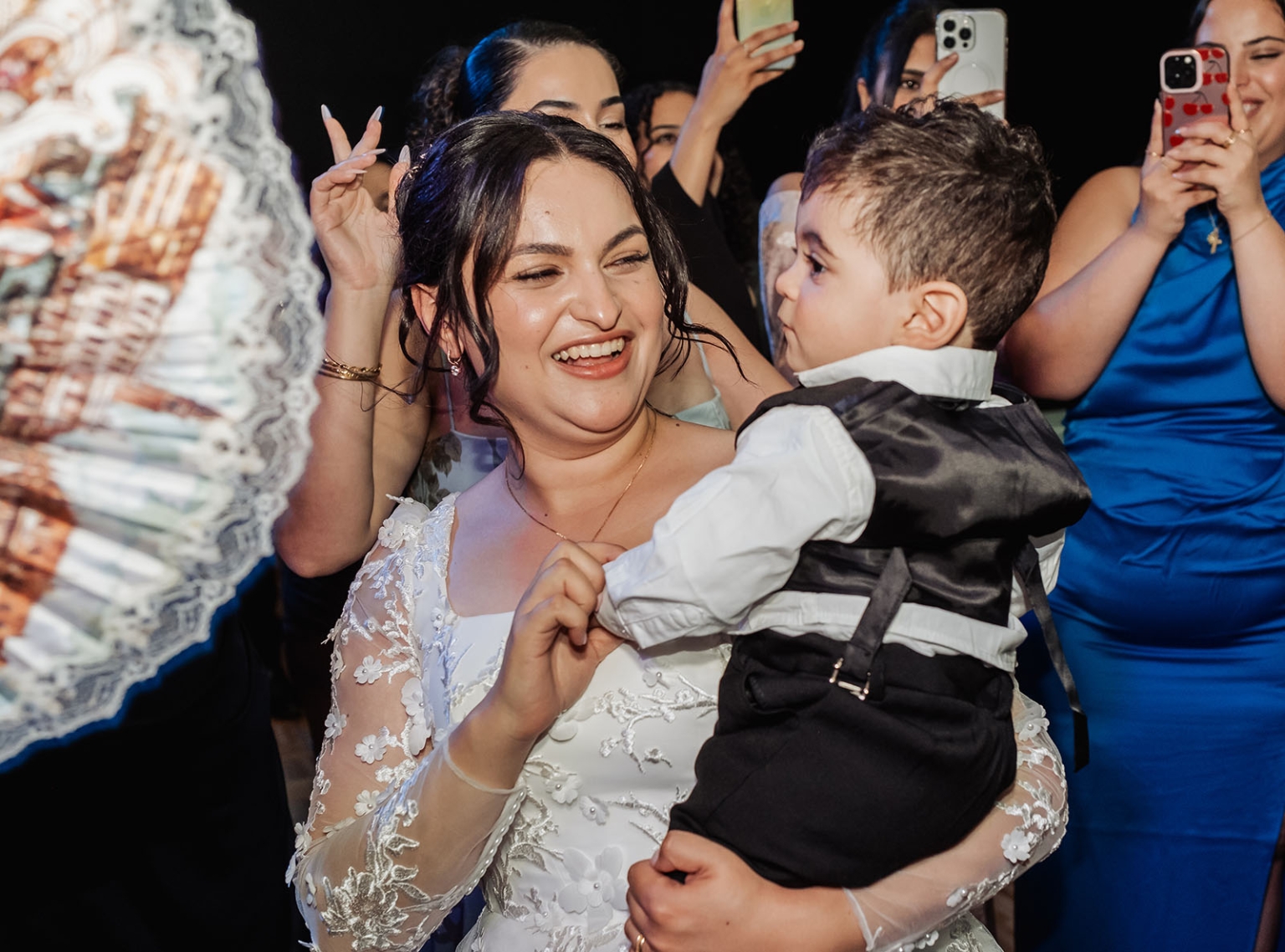 st george & st shenouda coptic church wedding - carmina & bill 89 Bride holding young boy during joyful wedding reception celebration.