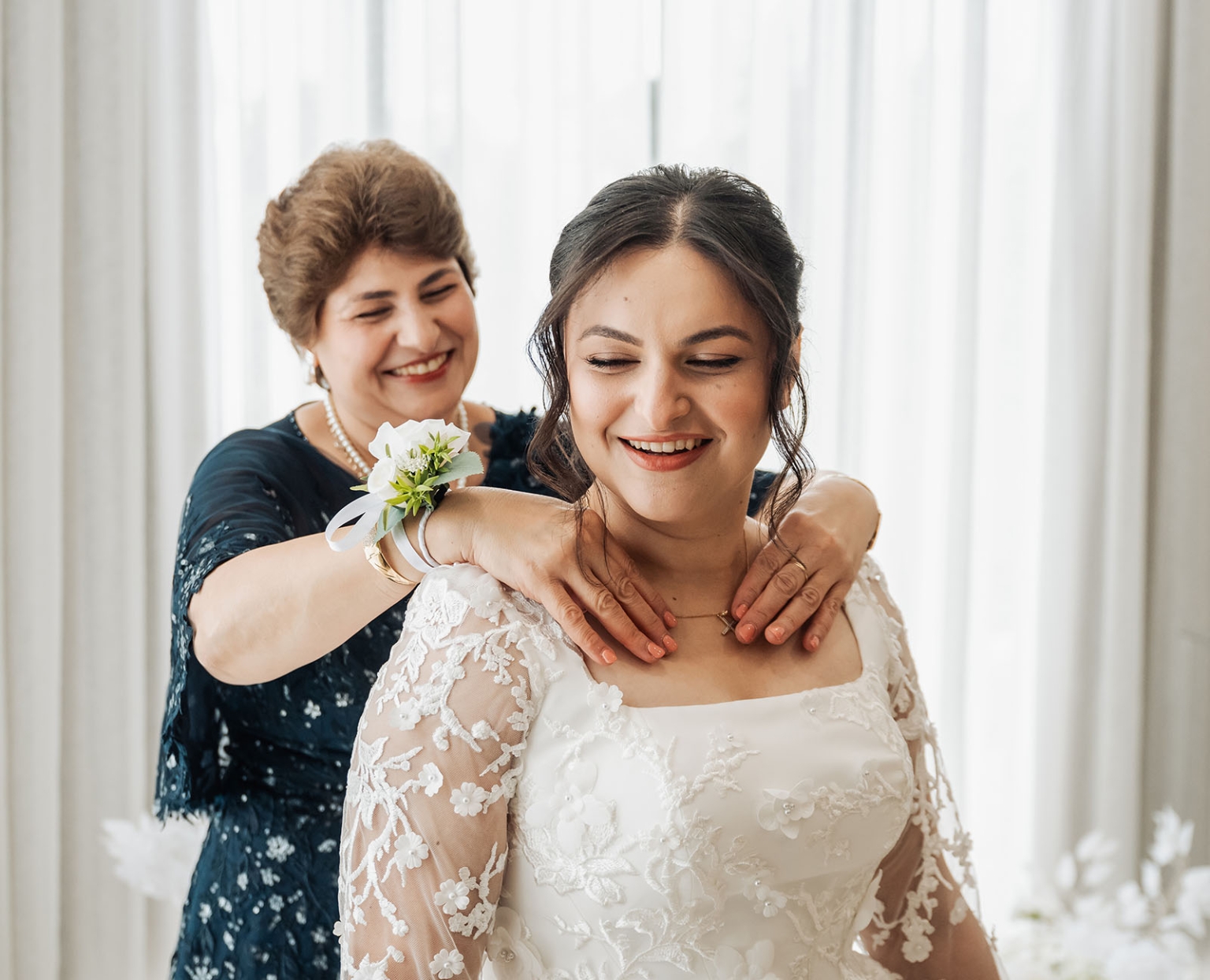 st george & st shenouda coptic church wedding - carmina & bill 26 Bride smiles as woman fastens necklace during wedding preparation.