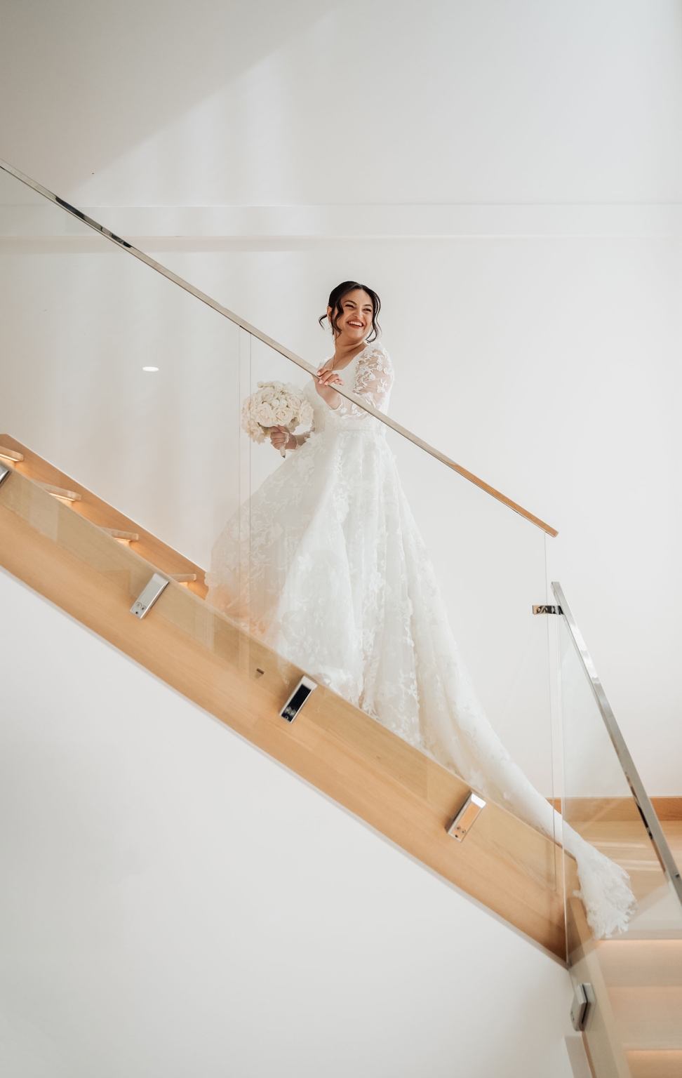 st george & st shenouda coptic church wedding - carmina & bill 31 Bride in lace wedding gown descending modern staircase with bouquet.