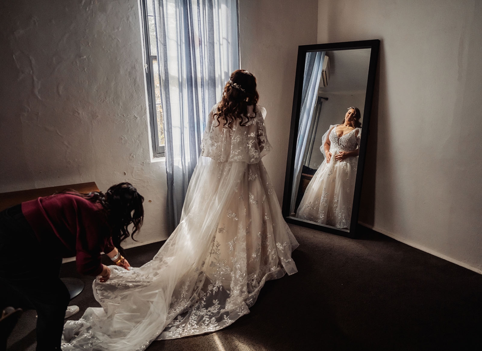 basket range wedding at the manor - leah & wes 7 Bride in lace wedding gown admiring mirror while attendant adjusts train.