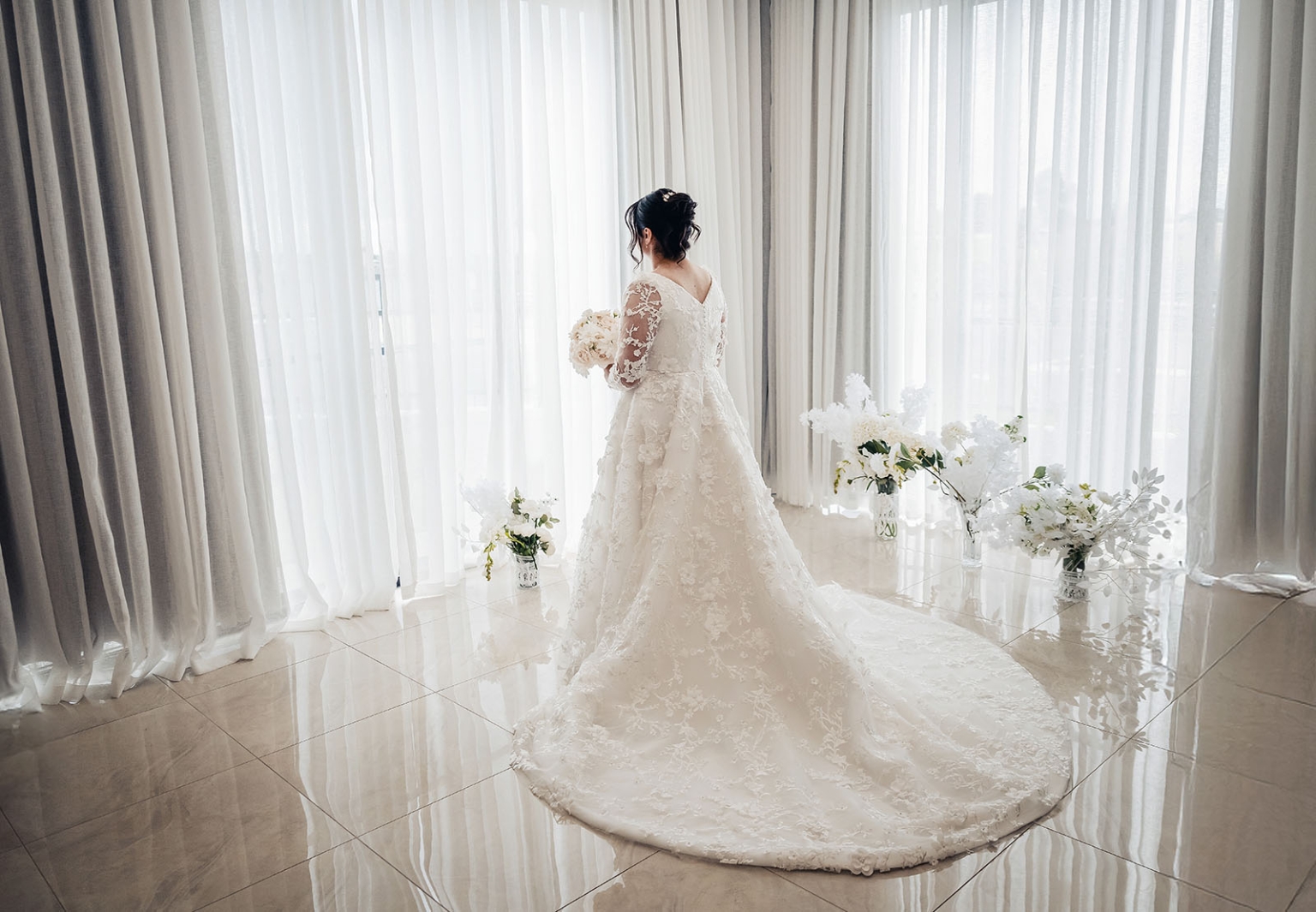 st george & st shenouda coptic church wedding - carmina & bill 27 Bride in lace wedding gown by window with bouquet and floral décor.