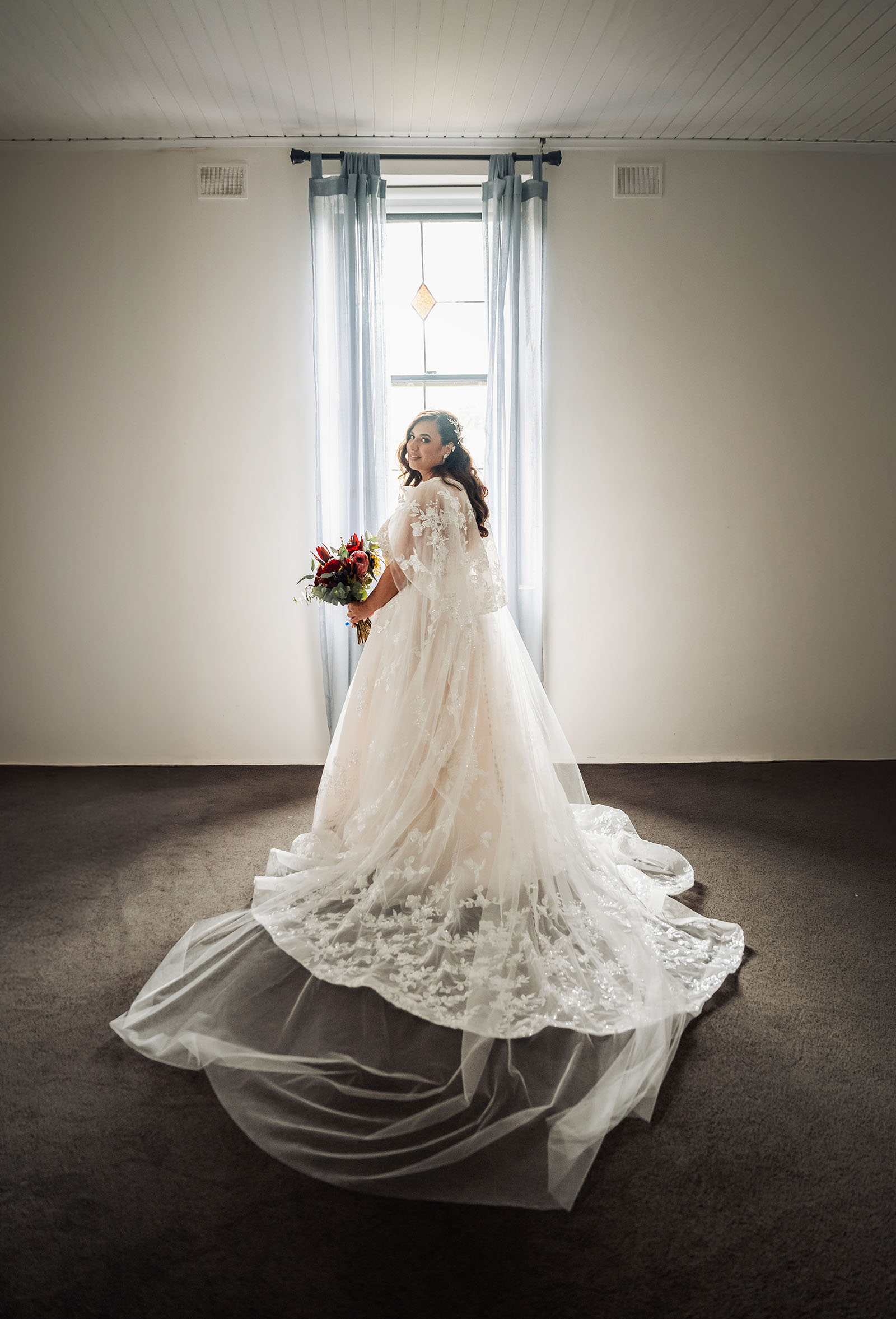 sunlit bride in lace wedding gown with train Bride in lace wedding gown with dramatic train by sunlit window.