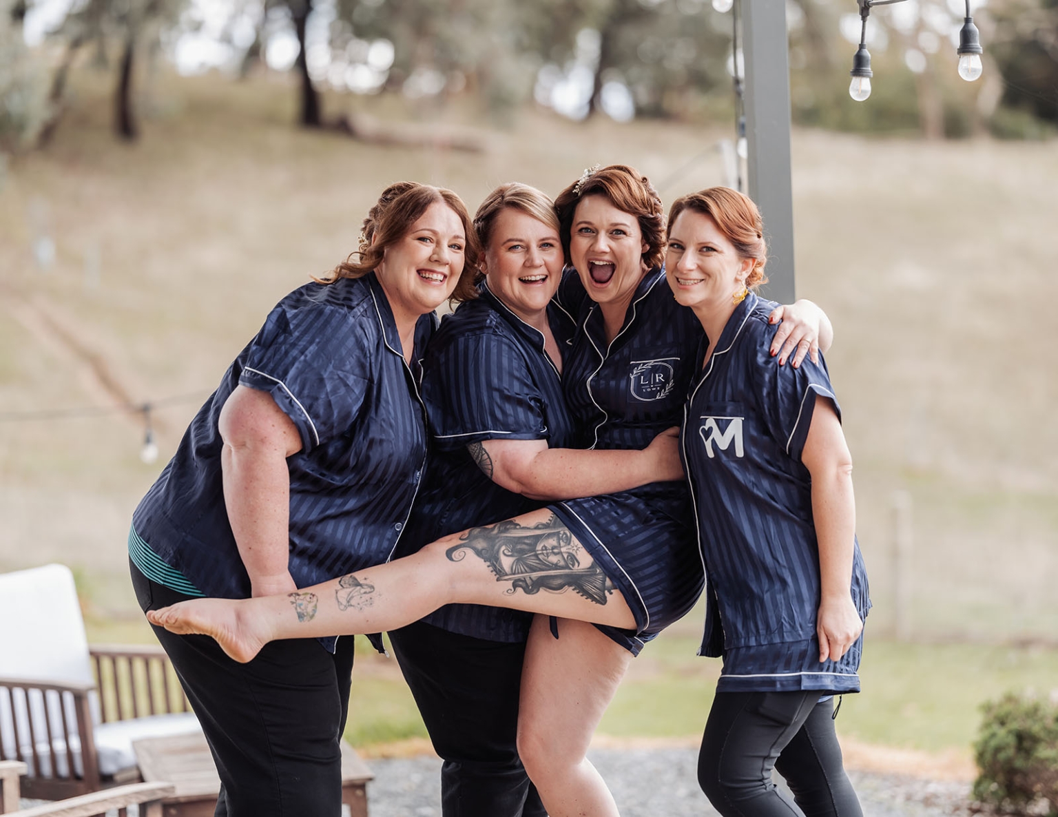 tiny house on the prairie wedding - lauren & bek 2 Bridesmaids in matching navy satin pajamas laughing at an outdoor wedding venue.