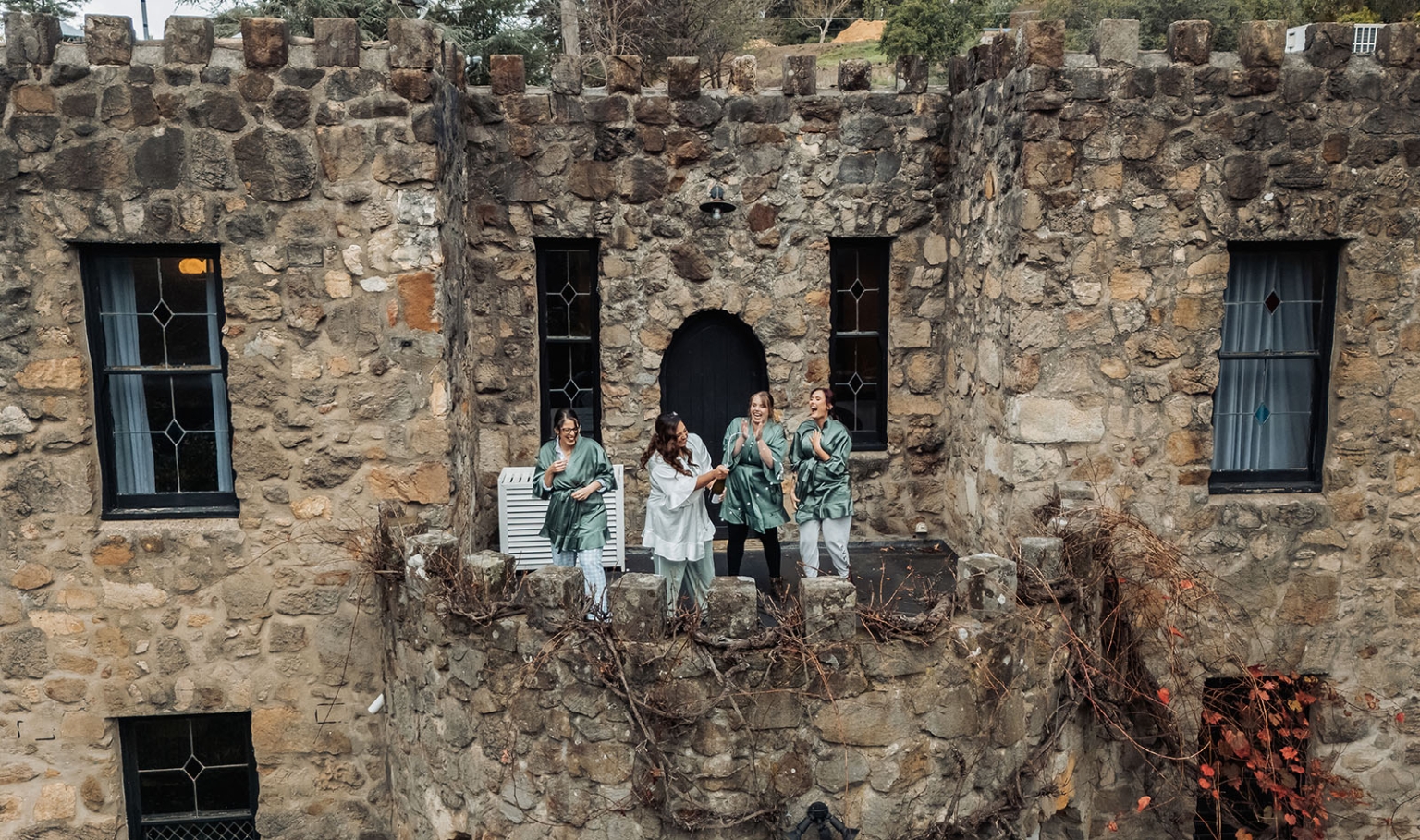 basket range wedding at the manor - leah & wes 4 Bridal party in green robes celebrating on a historic castle balcony.