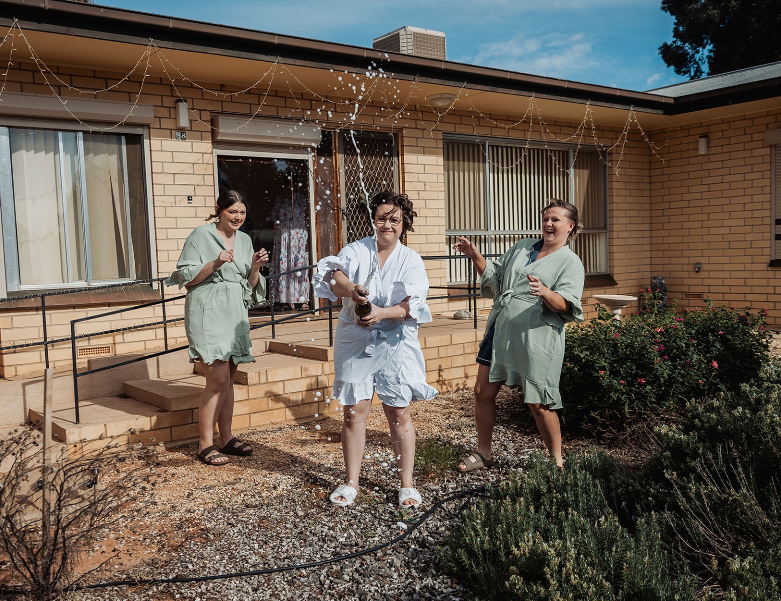 loxton's st peter's church wedding - madeline & brayden 21 Bride and bridesmaids celebrate with champagne spray outside brick house.