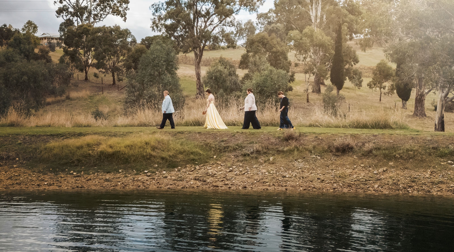 tiny house on the prairie wedding - lauren & bek 43 Bride and wedding party walk beside a rural lakeside countryside wedding venue.