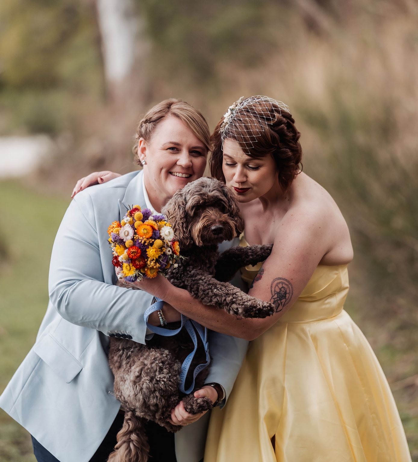 tiny house on the prairie wedding - lauren & bek 40 Wedding couple holding curly dog with colorful bouquet in outdoor portrait.