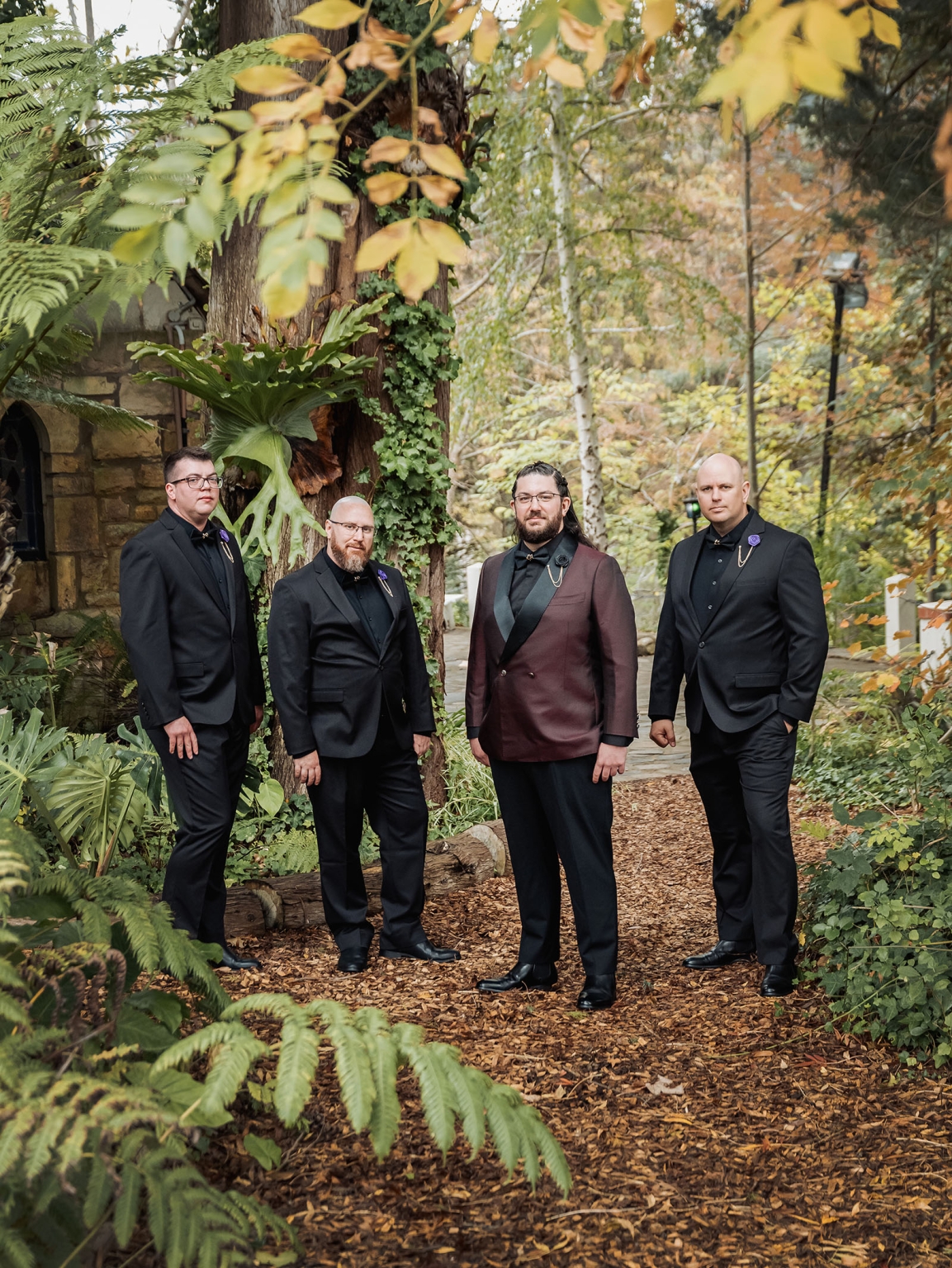 basket range wedding at the manor - leah & wes 27 Formal groomsmen portrait in burgundy and black suits in a woodland garden.