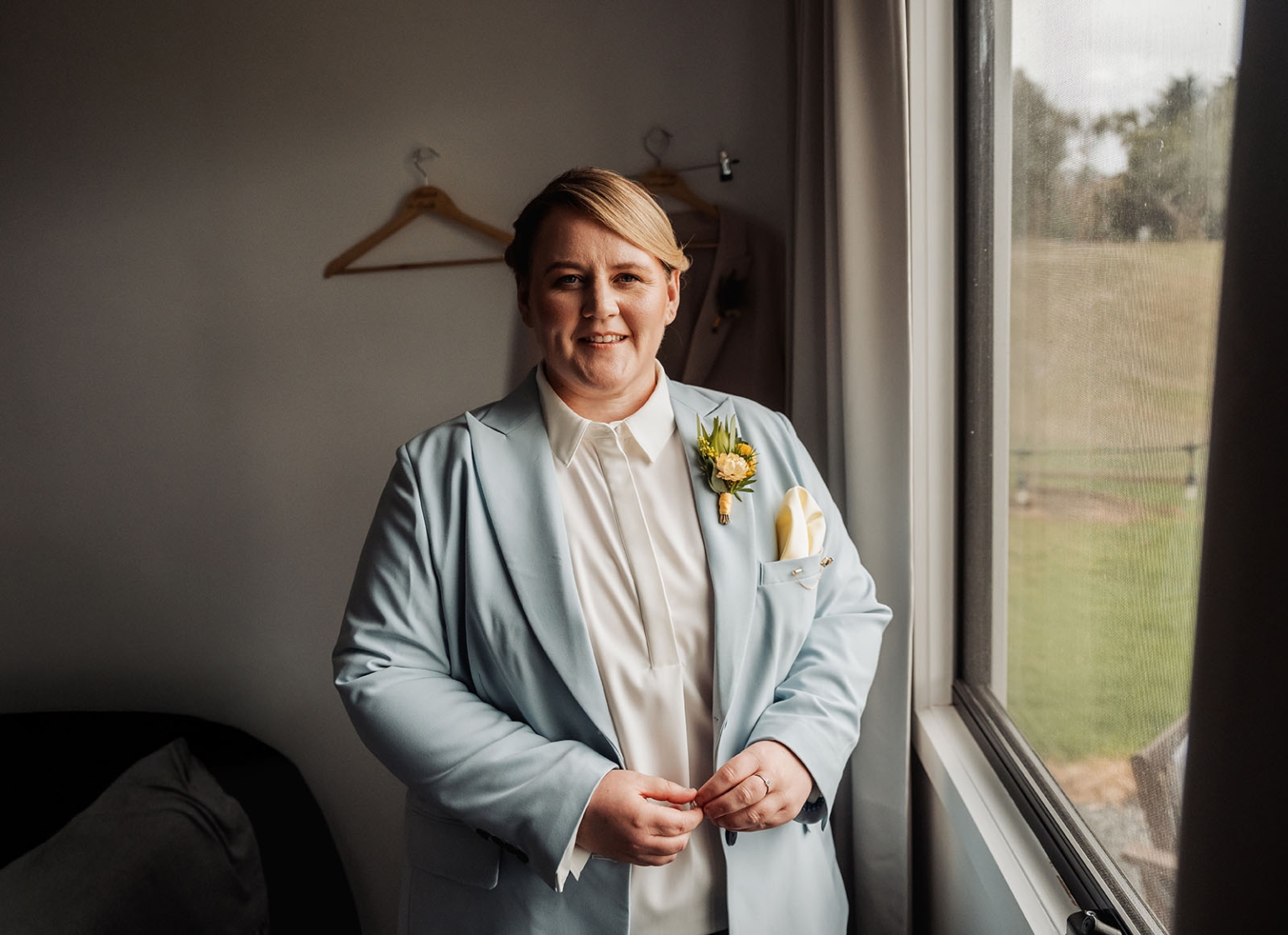 tiny house on the prairie wedding - lauren & bek 10 Groom in pale blue wedding suit posing by window with boutonniere.