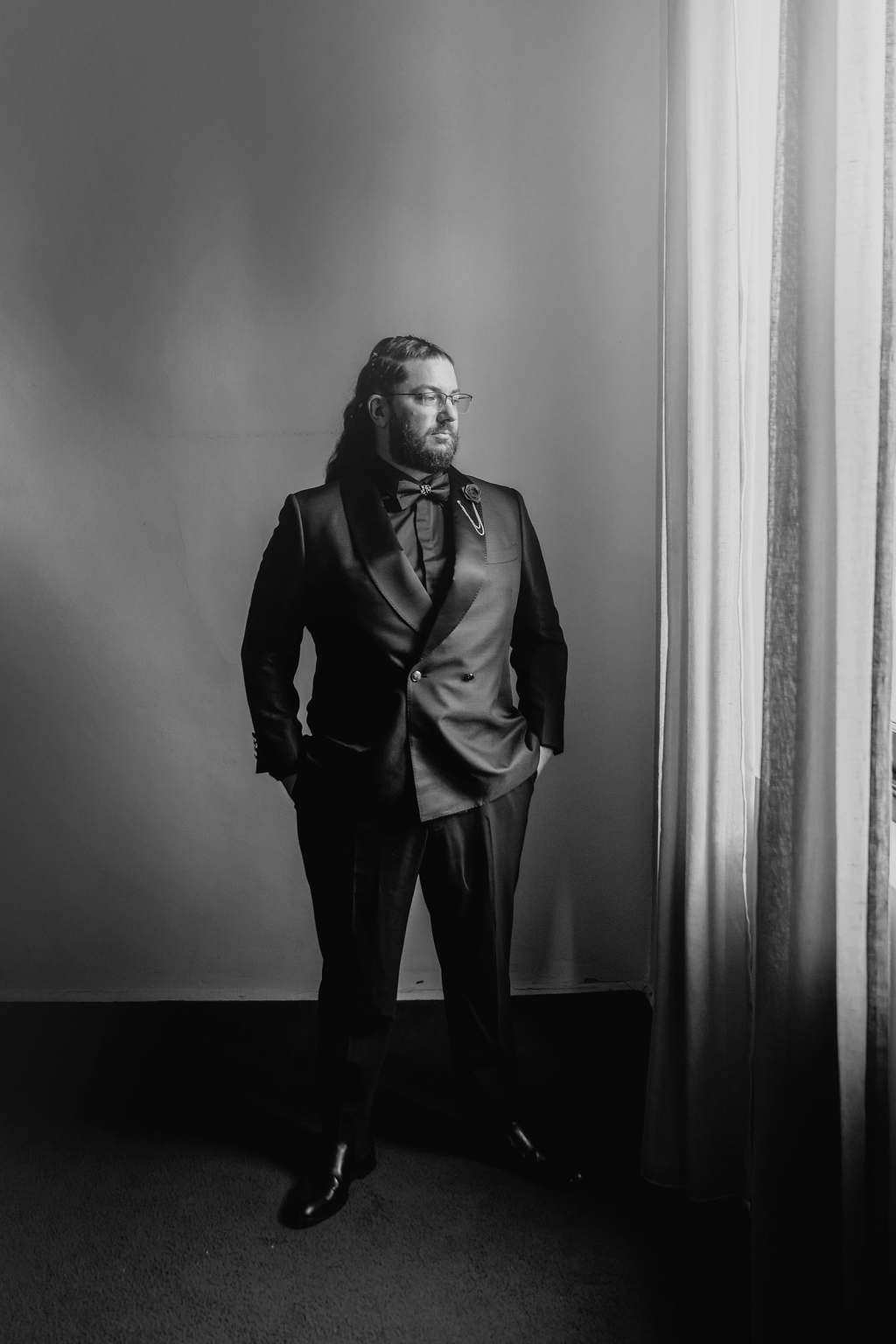 basket range wedding at the manor - leah & wes 26 Black-and-white formal portrait of bearded man in tuxedo by window.