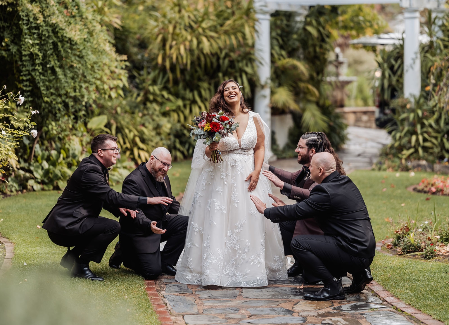 basket range wedding at the manor - leah & wes 31 Bride laughing with groomsmen in lush garden wedding portrait.