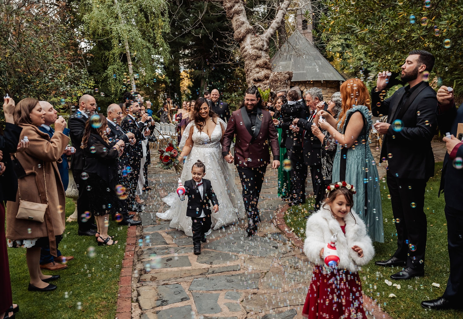 basket range wedding at the manor - leah & wes 53 Bride and groom celebrate a garden wedding bubble exit with family and flower children.
