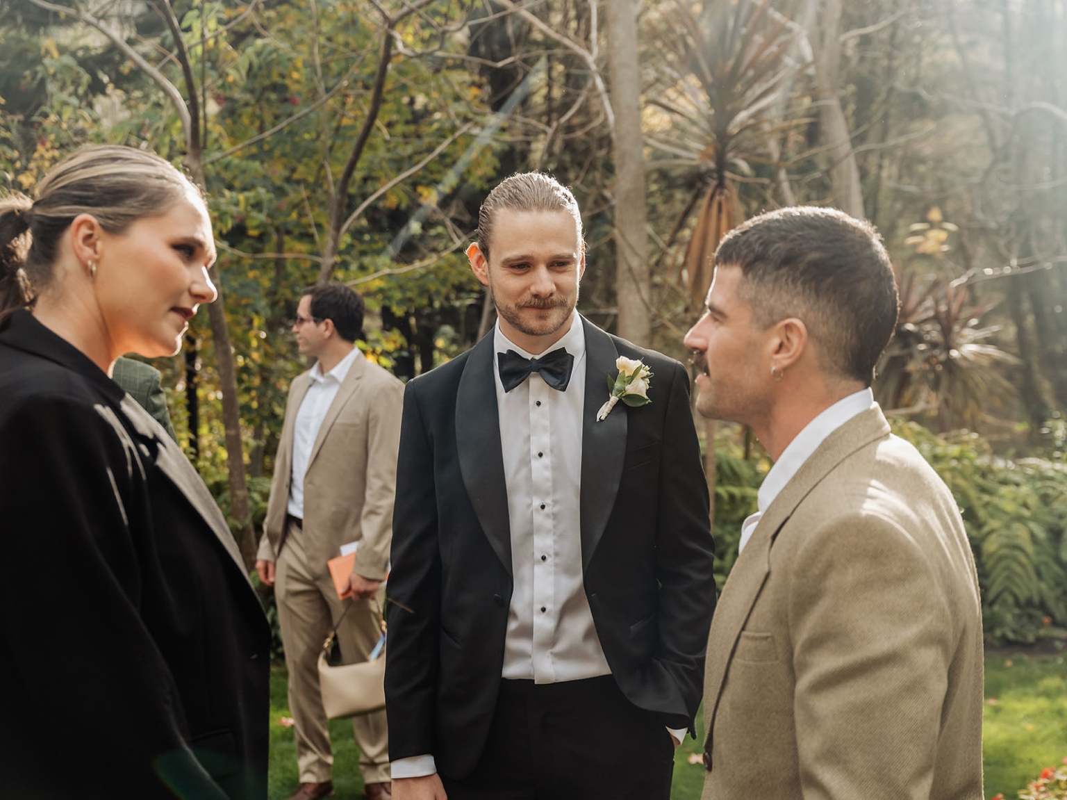 the manor wedding - crystal & mackenzie 45 Elegant garden wedding guests in tuxedo and beige suits during outdoor celebration.