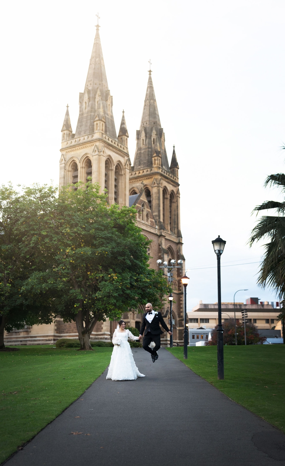 st george & st shenouda coptic church wedding - carmina & bill 72 Joyful wedding couple outside a Gothic cathedral in lush garden grounds.