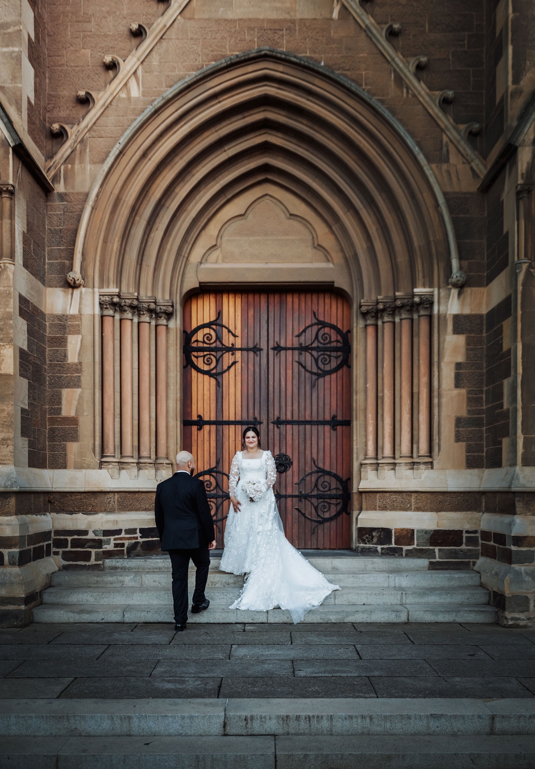st george & st shenouda coptic church wedding - carmina & bill 68 Bride and groom at Gothic church entrance for elegant wedding portrait.