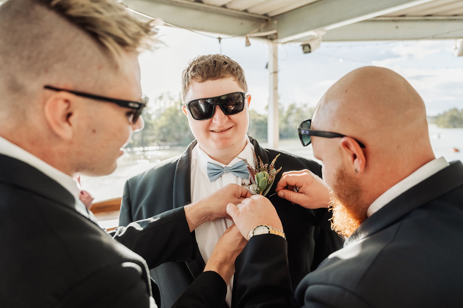 loxton's st peter's church wedding - madeline & brayden 9 Groomsmen pin boutonniere on groom during outdoor wedding preparation.