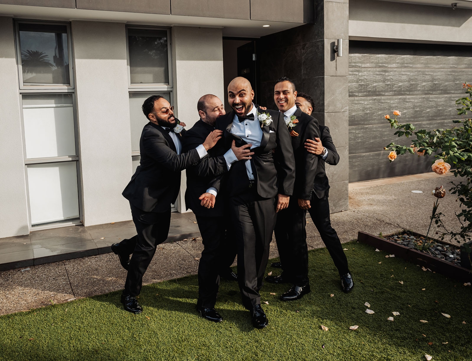 st george & st shenouda coptic church wedding - carmina & bill 12 Groom and groomsmen laughing in black tuxedos during modern outdoor wedding portrait.