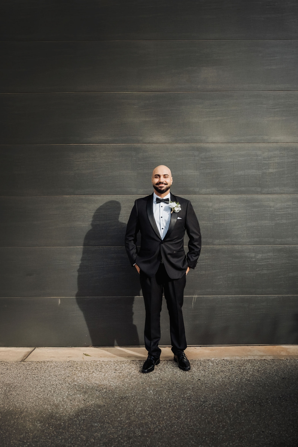 st george & st shenouda coptic church wedding - carmina & bill 15 Groom in black tuxedo posing against modern dark wall.