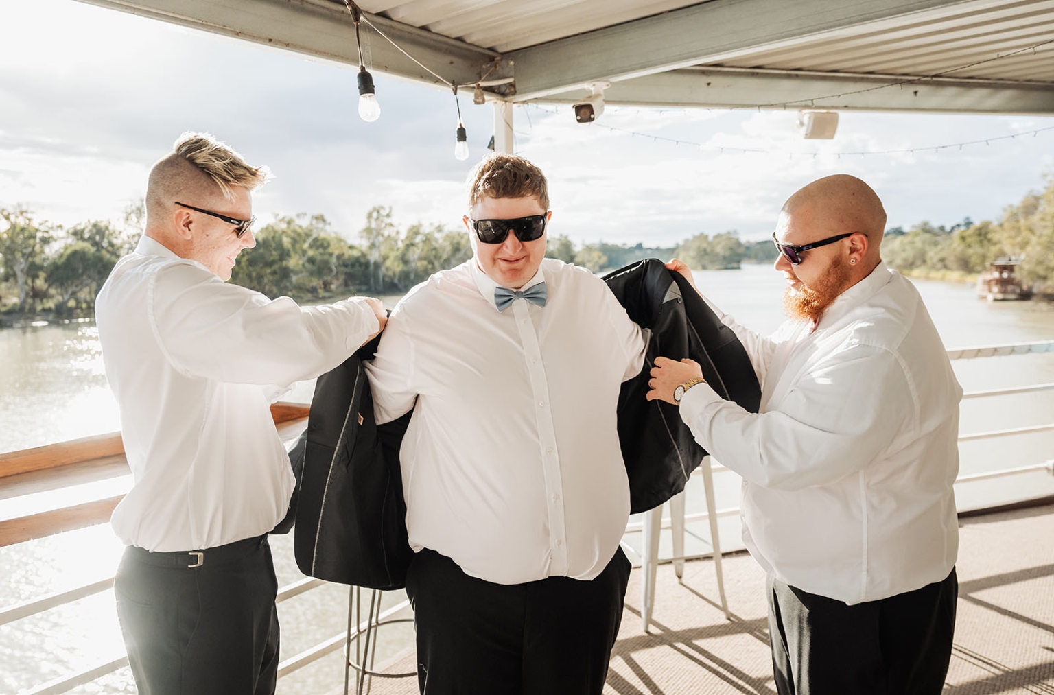 loxton's st peter's church wedding - madeline & brayden 7 Groomsmen help groom with suit jacket on riverside wedding deck.
