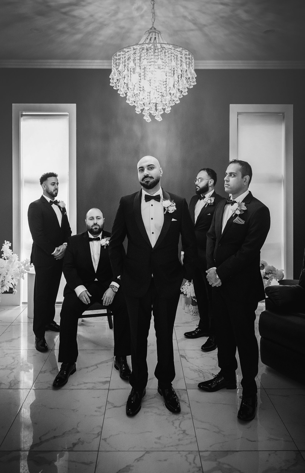 st george & st shenouda coptic church wedding - carmina & bill 13 Elegant black-and-white groomsmen tuxedo portrait under chandelier in luxury wedding venue.