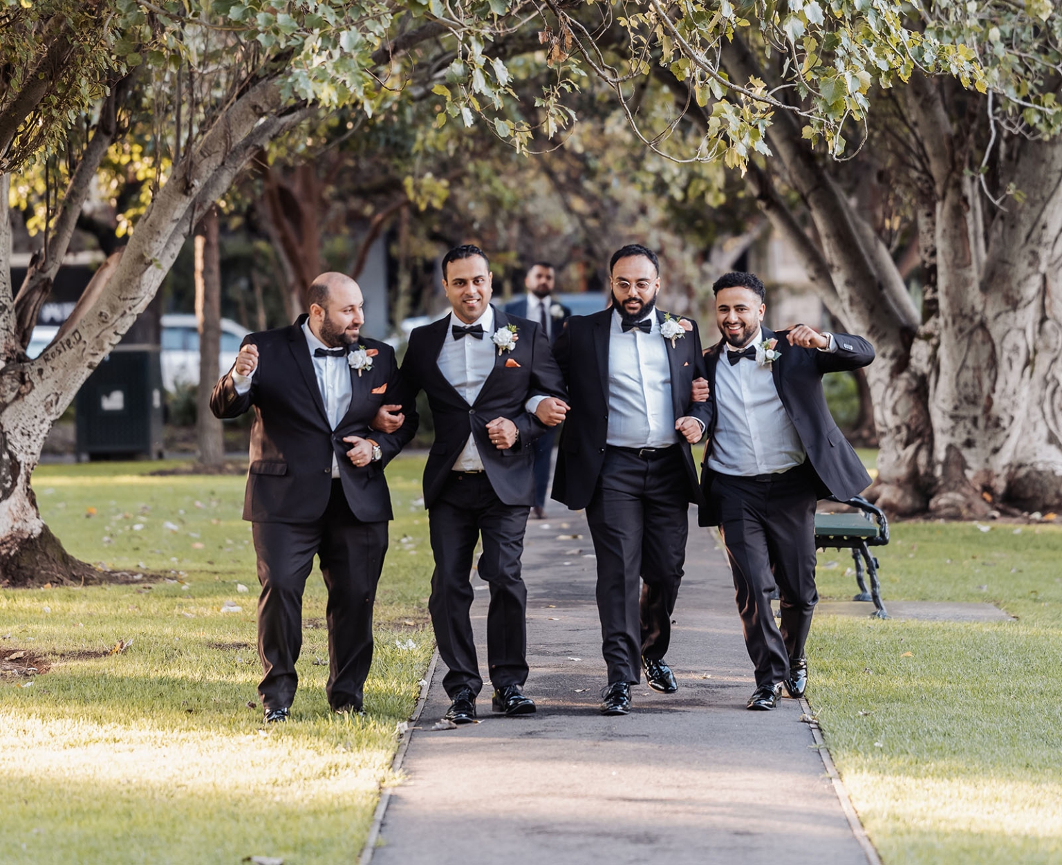 st george & st shenouda coptic church wedding - carmina & bill 61 Groomsmen in black tuxedos walking together through a leafy park.