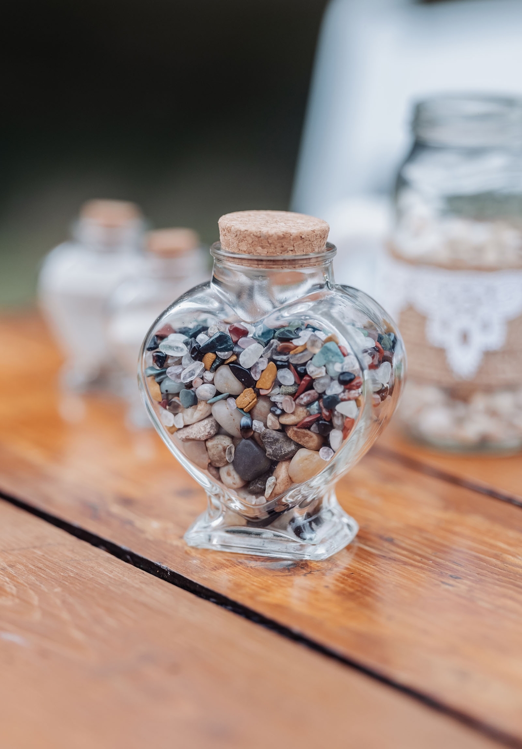 tiny house on the prairie wedding - lauren & bek 24 Heart-shaped glass bottle filled with colorful polished stones on rustic wood.