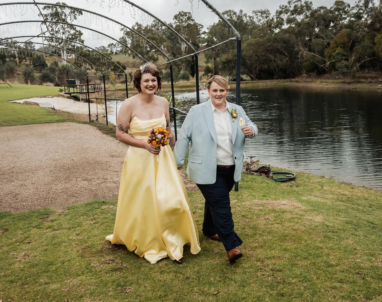 tiny house on the prairie wedding - lauren & bek 21 Wedding couple holding hands by a lakeside ceremony with flowers and string lights.
