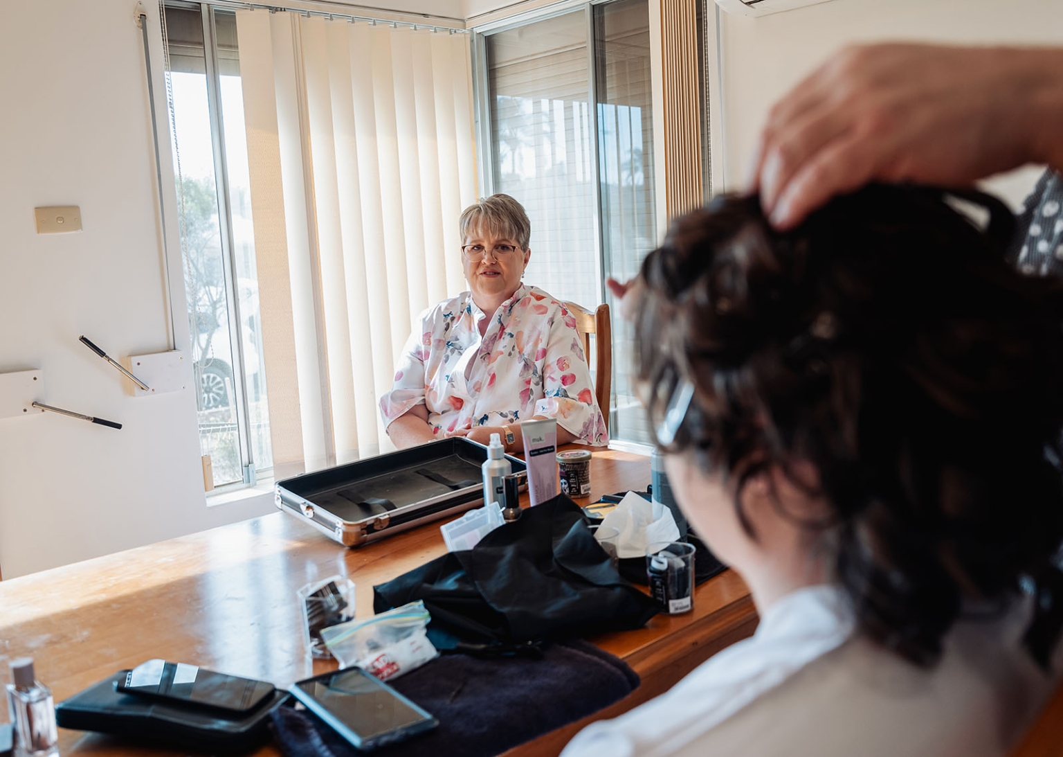 loxton's st peter's church wedding - madeline & brayden 22 Bridal makeup prep room with woman by sunny window and hairstyling station.