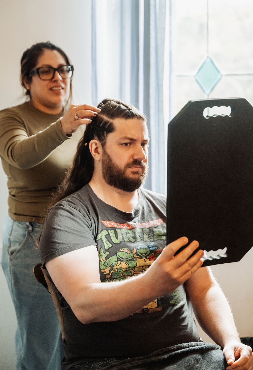 basket range wedding at the manor - leah & wes 16 Man checking cornrow braids in mirror during at-home hairstyling.