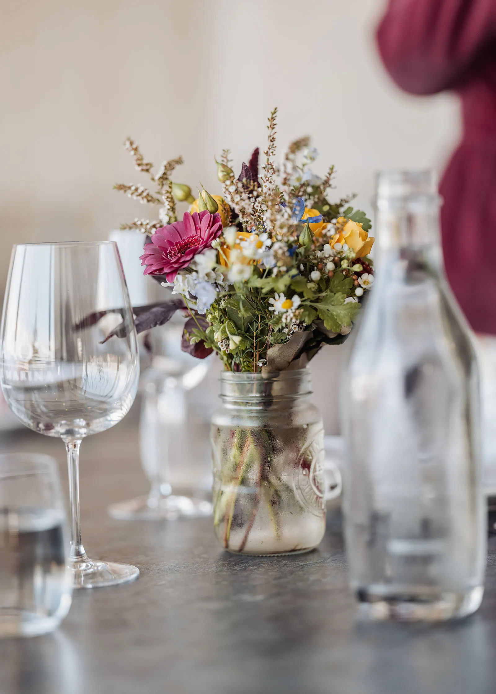 Mason jar floral centerpiece with pink daisies and yellow roses on reception table.