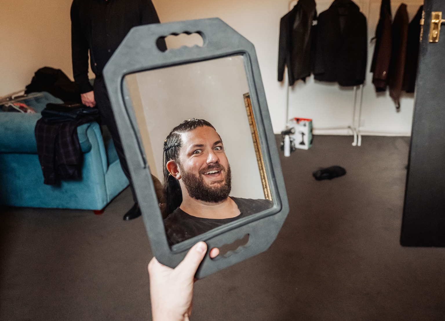 basket range wedding at the manor - leah & wes 15 Smiling bearded man reflected in handheld mirror backstage dressing room.