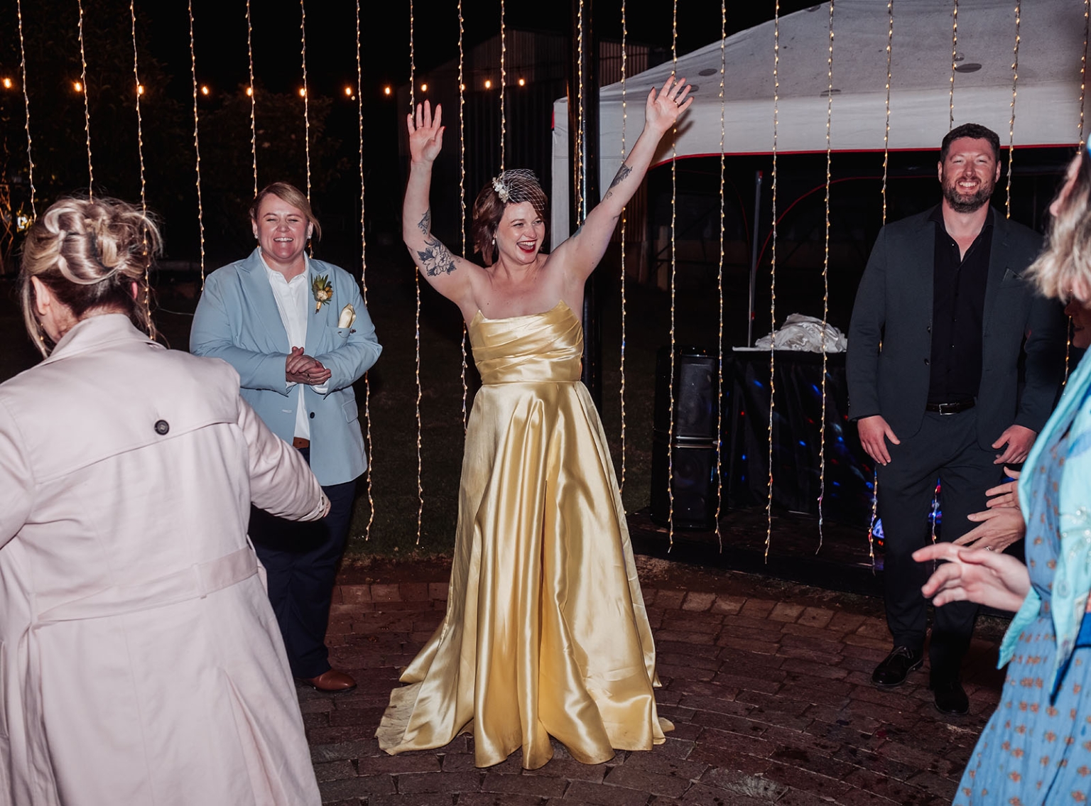 tiny house on the prairie wedding - lauren & bek 68 Woman in gold gown celebrating under string lights at nighttime wedding reception.