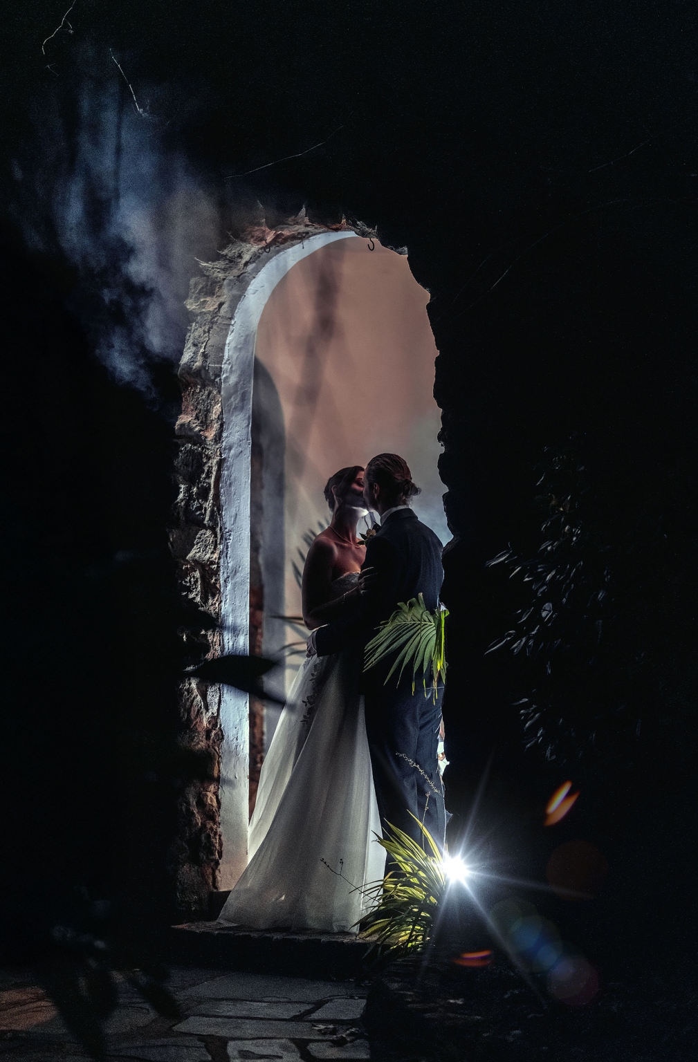 the manor wedding - crystal & mackenzie 98 Romantic nighttime wedding portrait of bride and groom kissing beneath a stone archway.