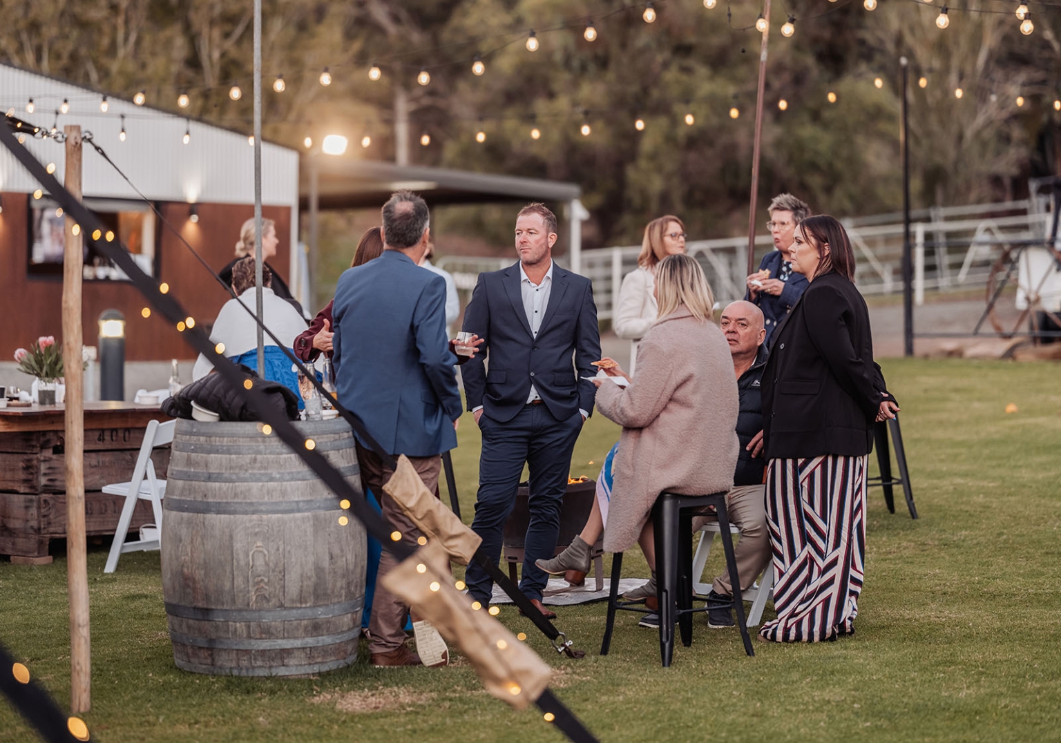 tiny house on the prairie wedding - lauren & bek 58 Elegant outdoor garden reception with string lights, wine barrels, and guests mingling.